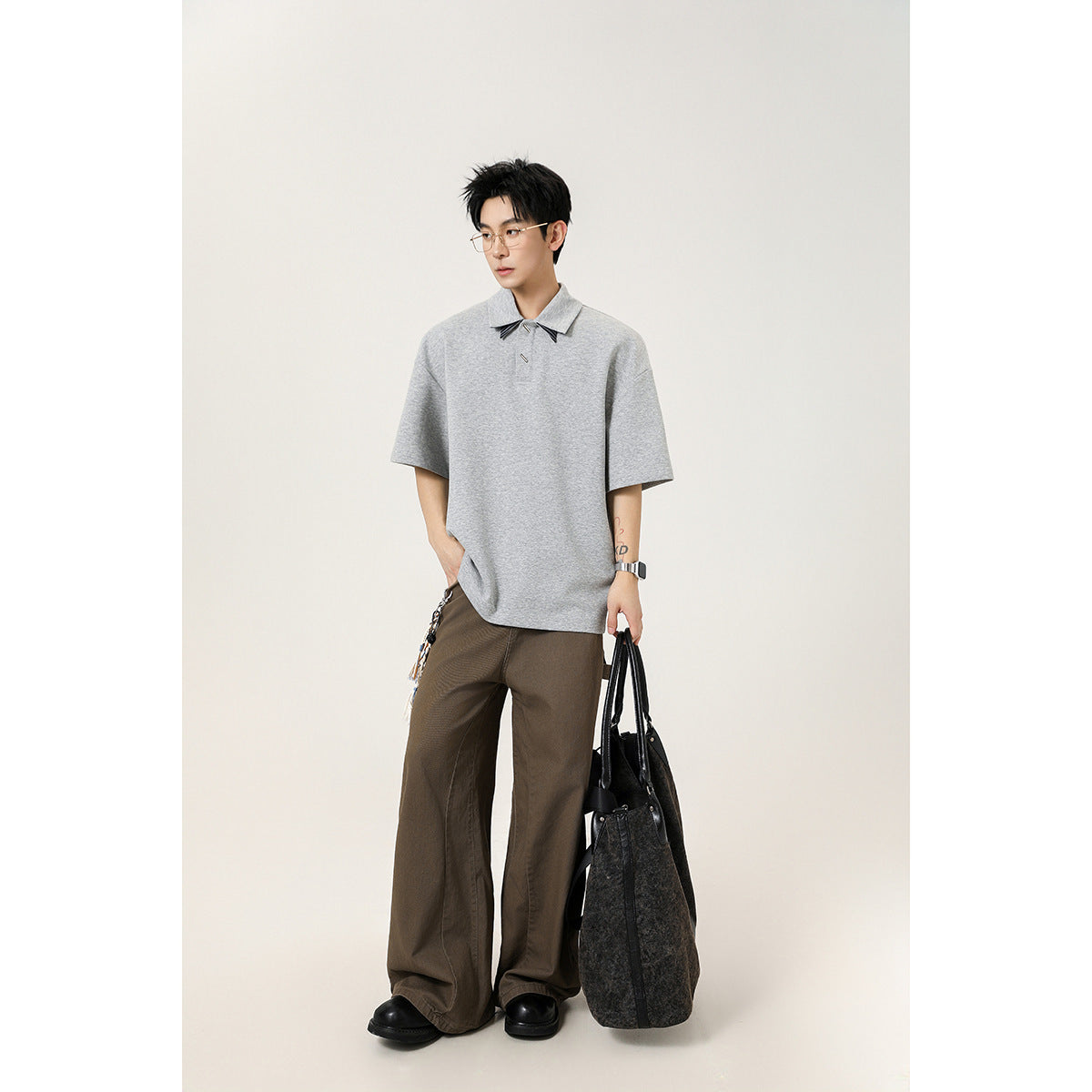 Full-length model wearing a heather-gray oversized short-sleeve polo with a pointed collar and decorative accents.