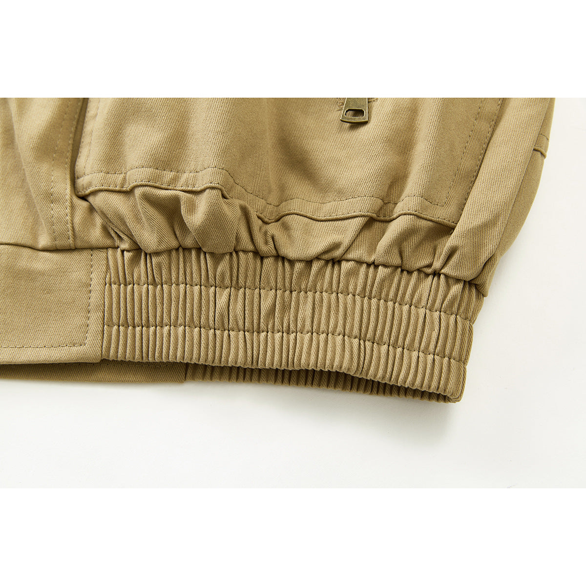 Close-up of a tan jacket's gathered elastic waistband and stitched hem panels.