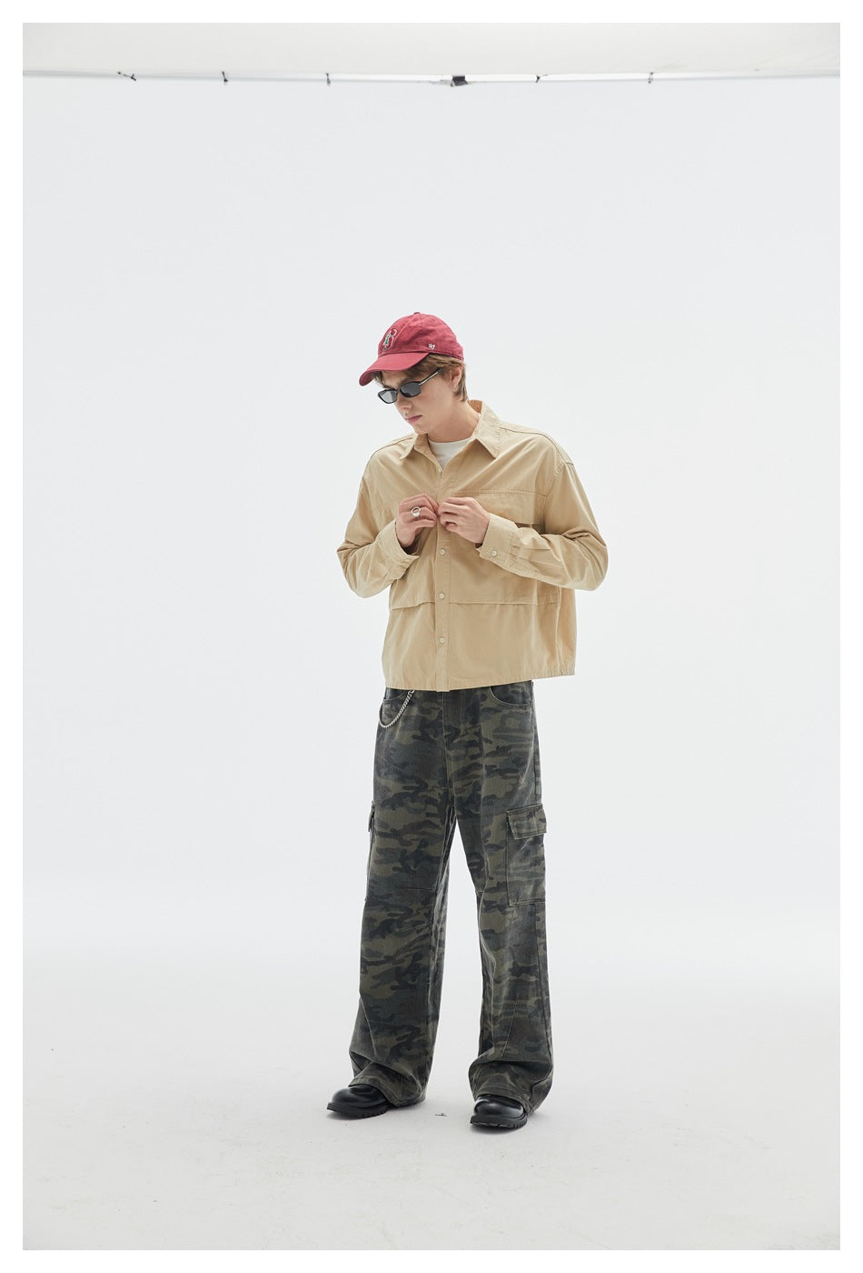 Model wearing a beige button-up shirt and loose dark camouflage cargo pants with side pockets.