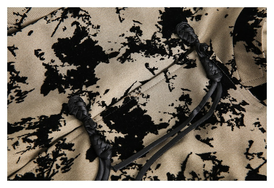 Close-up of tan and black abstract floral fabric with two black braided knot fasteners and hanging straps.