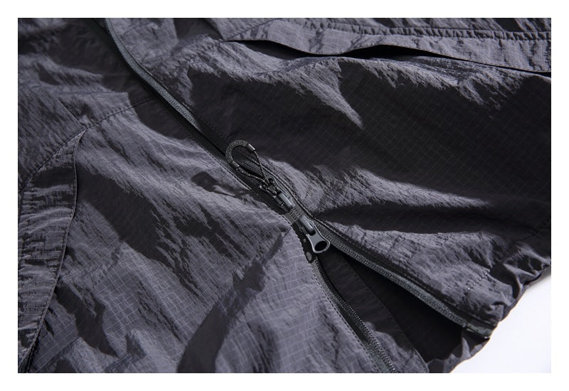 Close-up of crinkled charcoal-black garment fabric with a black zipper and two pull tabs.