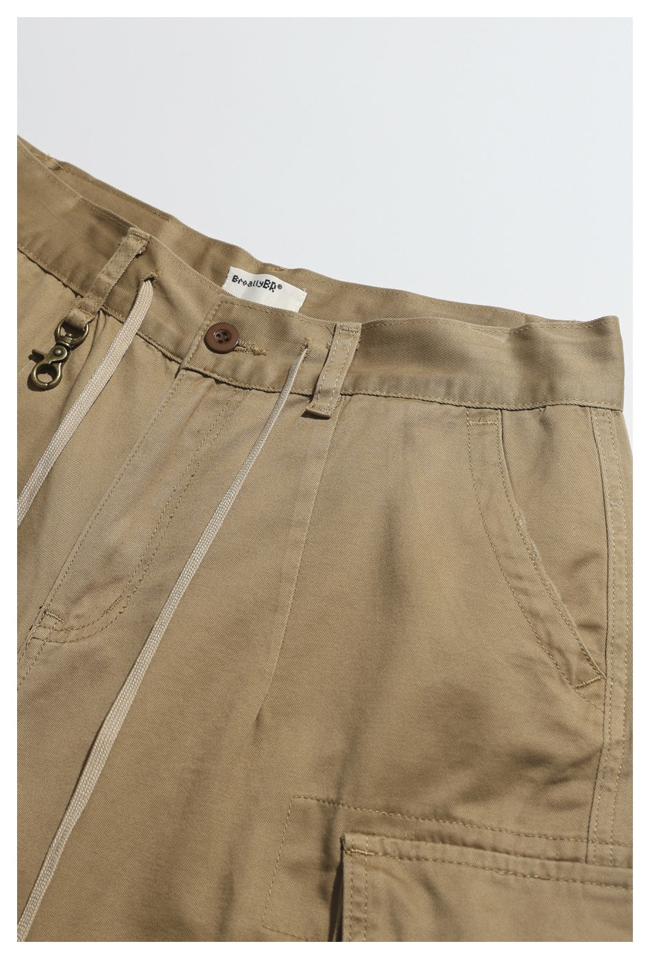 Close-up of tan shorts showing the buttoned waist, drawstring, belt loop, and front pocket stitching.