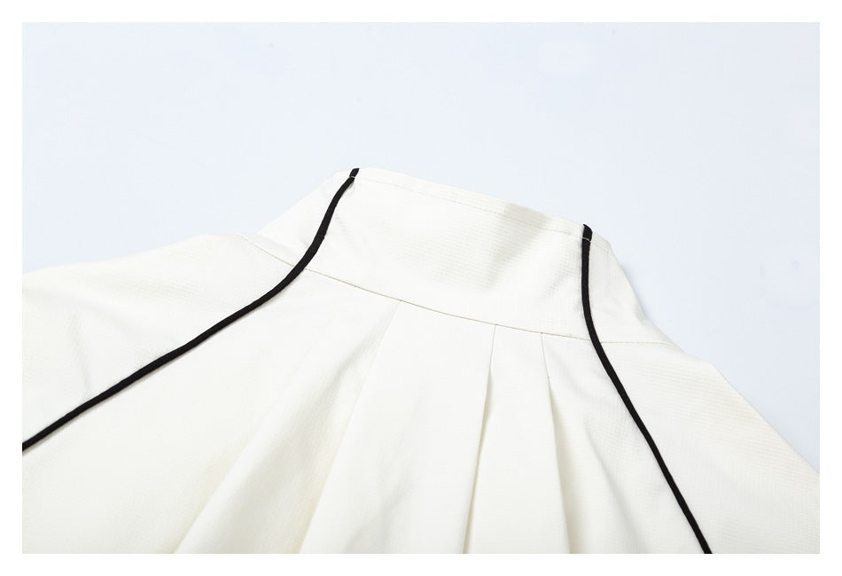 Close-up of the ivory garment's back yoke, with black piping and pleats below.
