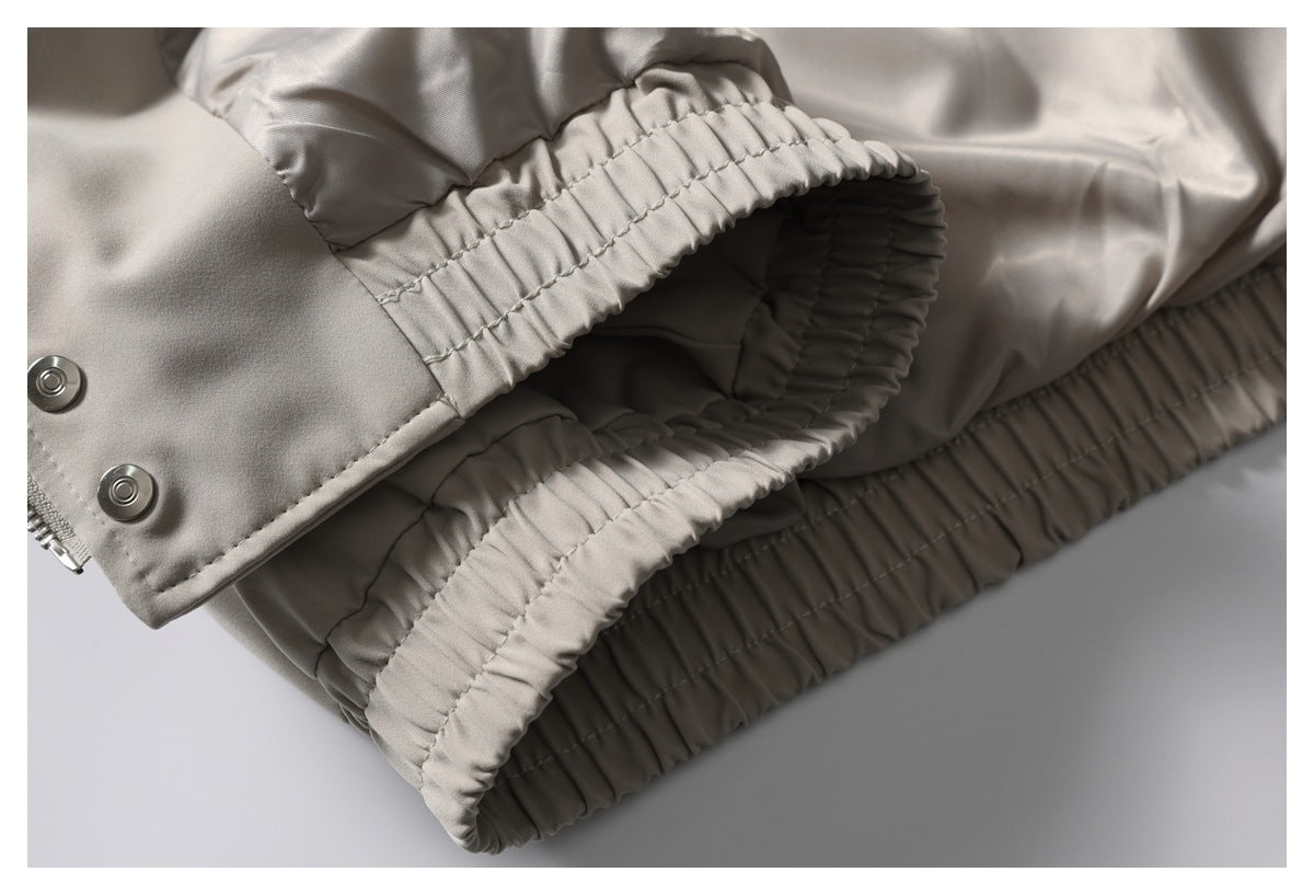 Close-up of taupe trousers showing a gathered elastic waistband, zipper, and metal snaps.