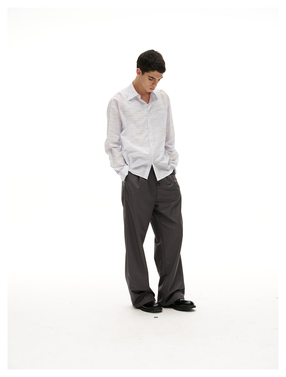 Model looking down in a light striped button-up shirt with hands in pockets, wearing gray wide-leg trousers