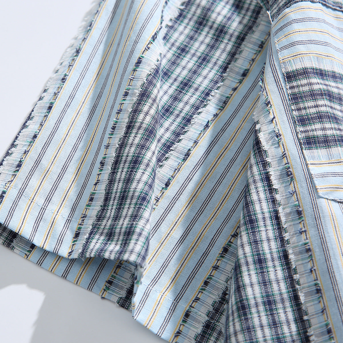 Close-up of pale blue, navy, and white striped and plaid shirt fabric with frayed panel seams.