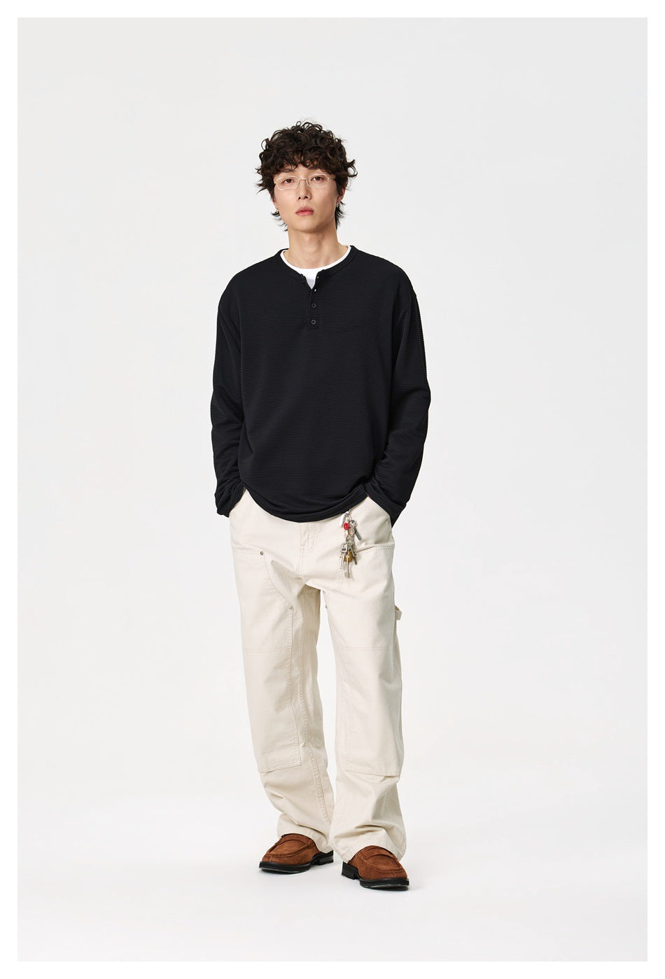 Model wearing a black long-sleeve henley shirt with white pants, shown from the front.