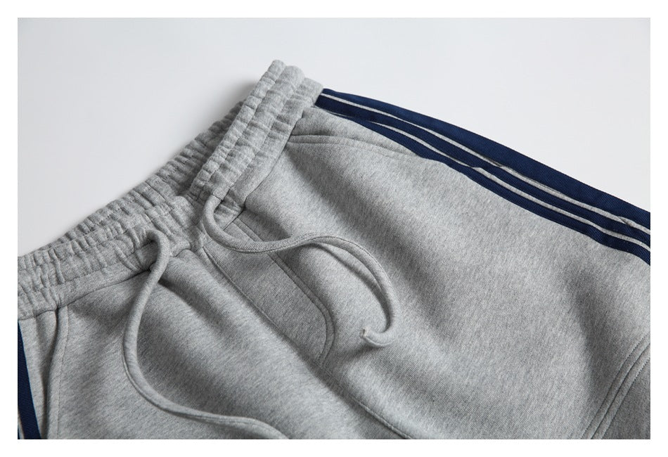 Close-up of gray sweatpants showing the elastic waistband, drawstring, pocket opening, and navy side stripes.