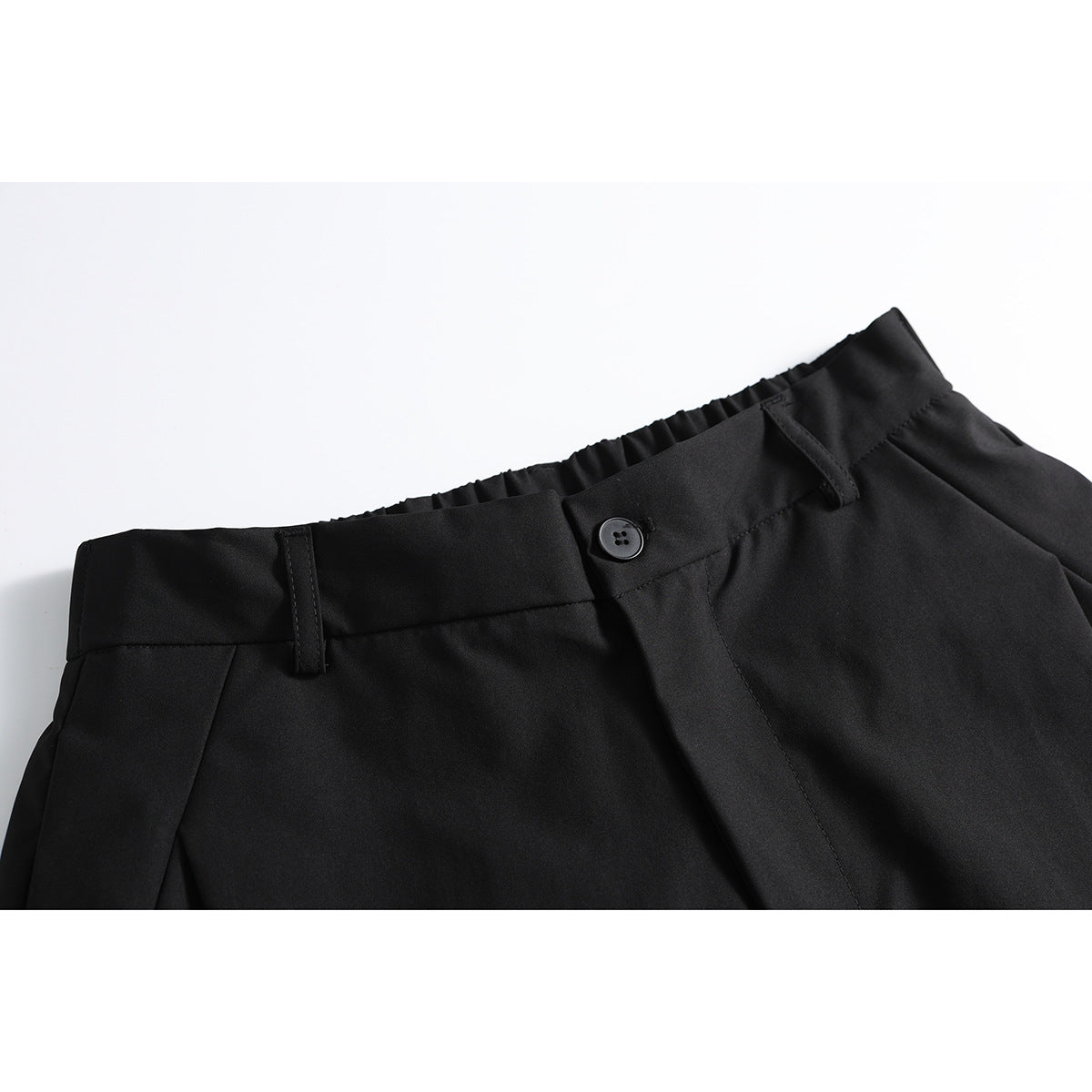 Close-up of black shorts showing the waistband, belt loops, button, and front pleat.