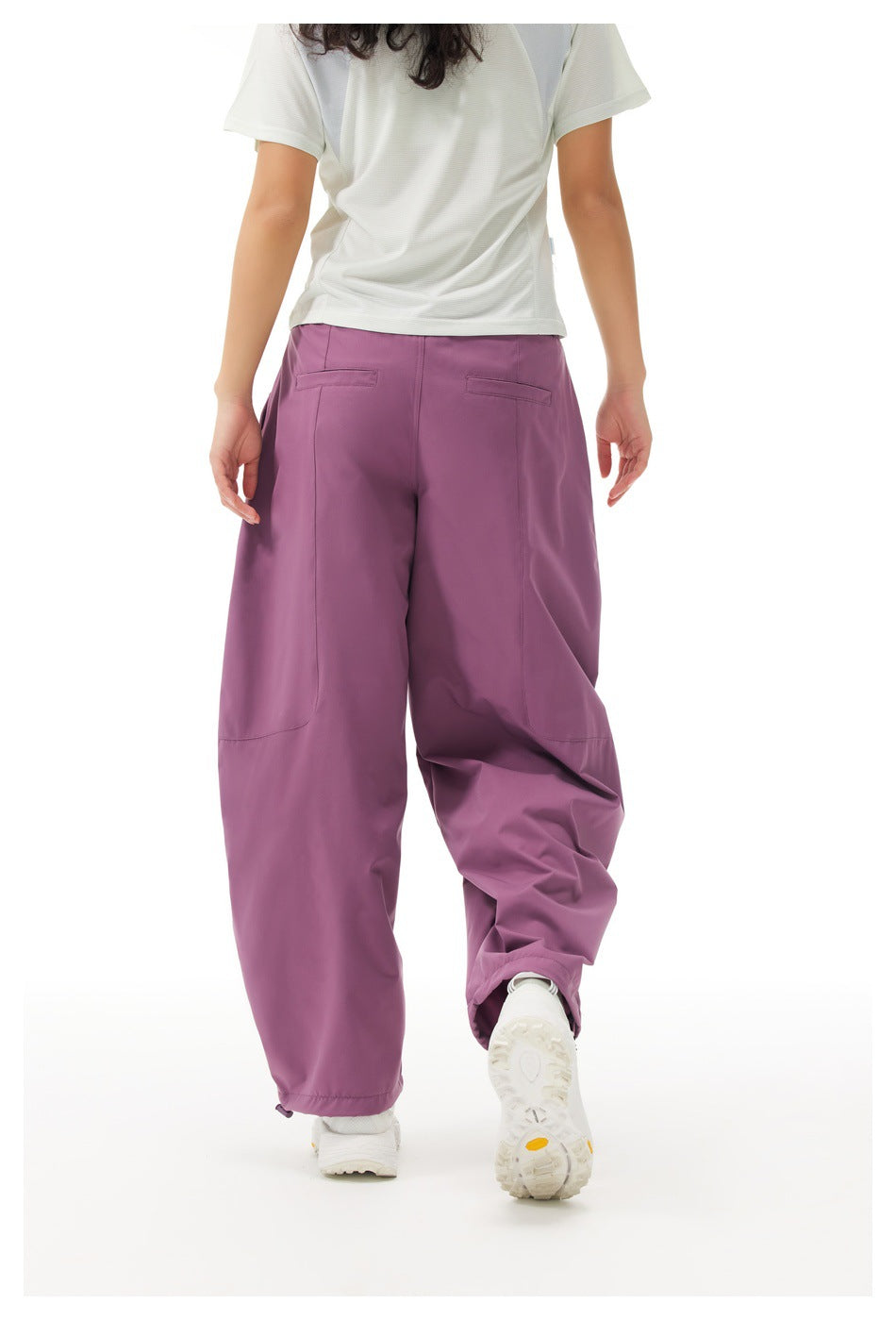 Rear view of a model wearing loose plum-purple pants with small back pockets and a white short-sleeve shirt.