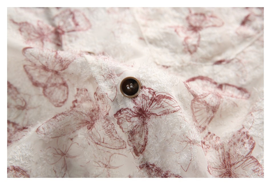 Close-up of a dark button on ivory textured fabric printed with dusty rose butterflies.