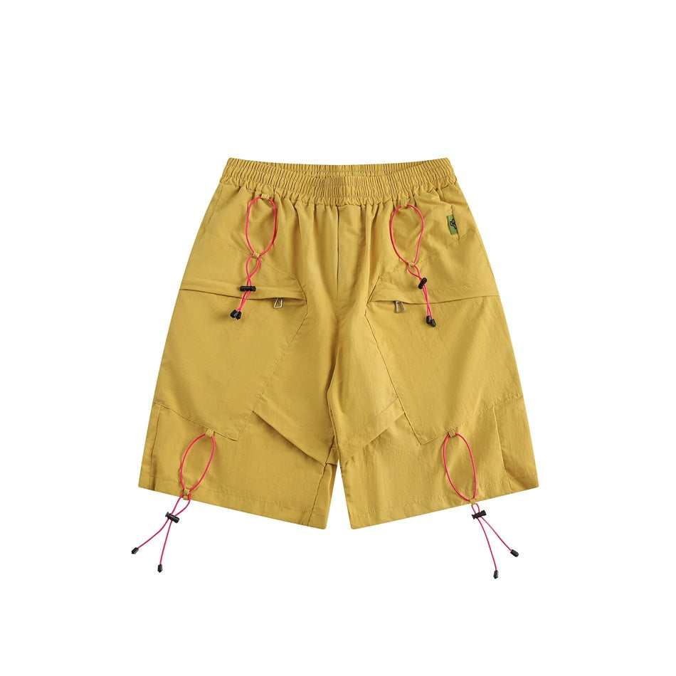 Yellow knee-length shorts, front view, with pink toggle cords, angled flap panels and an elastic waistband