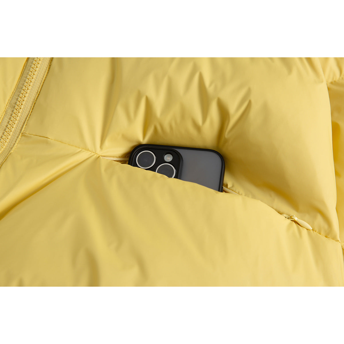 Close-up of a phone tucked into a pocket on a yellow puffer jacket.