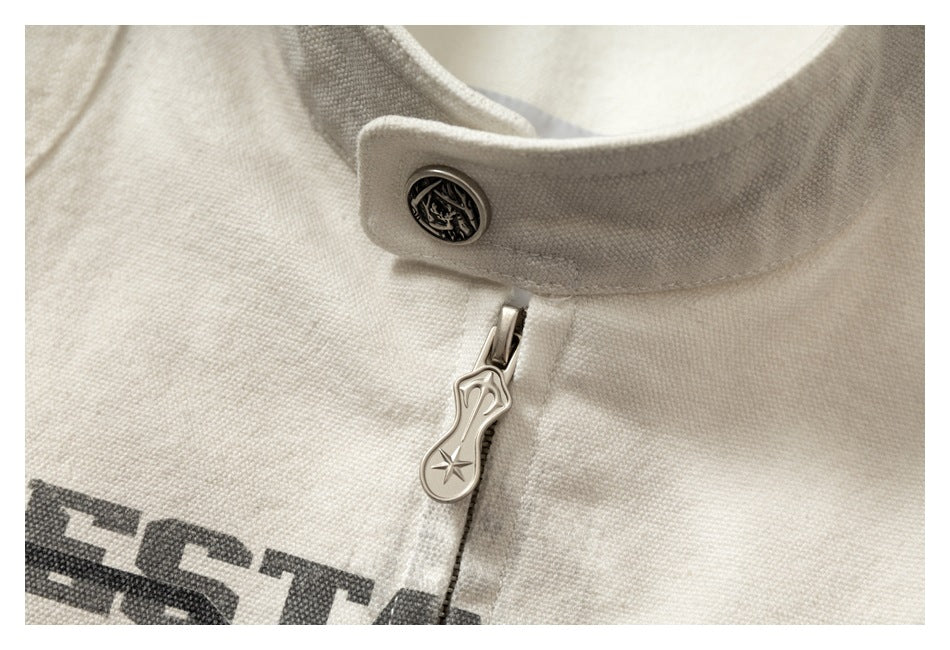 Close-up of the jacket's stand-collar snap, metal zipper pull and dark printed lettering on off-white fabric.