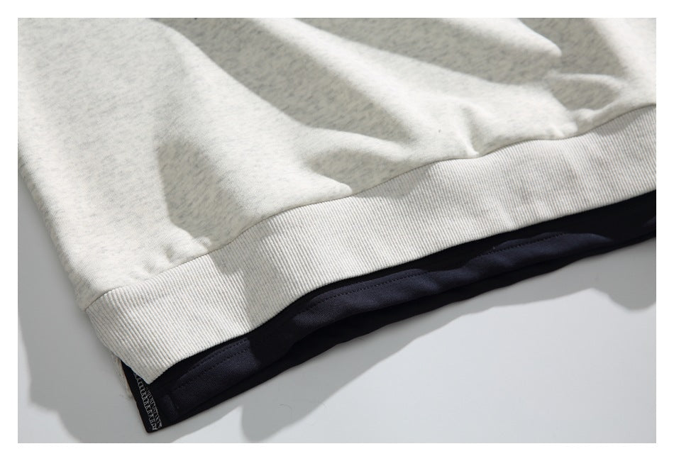 Close-up of the ribbed bottom hem and dark fabric layer beneath the off-white sweatshirt.