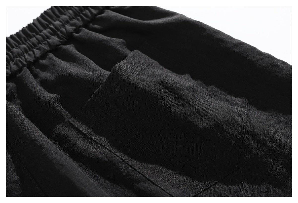 Close-up of a black garment showing a gathered elastic waistband and stitched patch pocket.