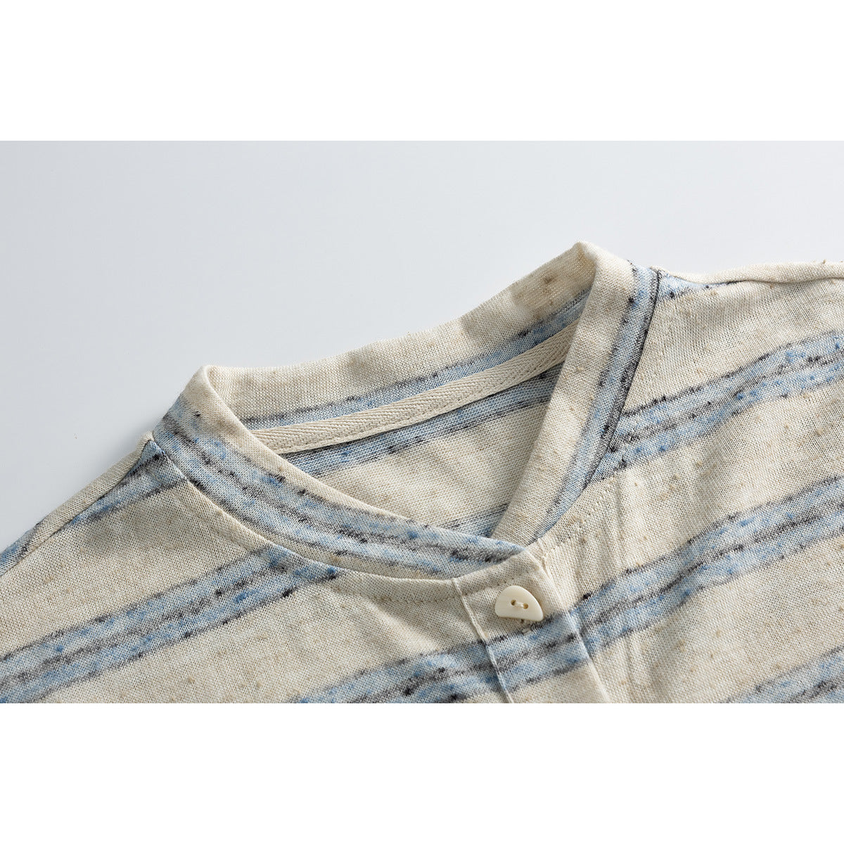 Close-up of a cream and blue striped top's neckline and single-button front placket.