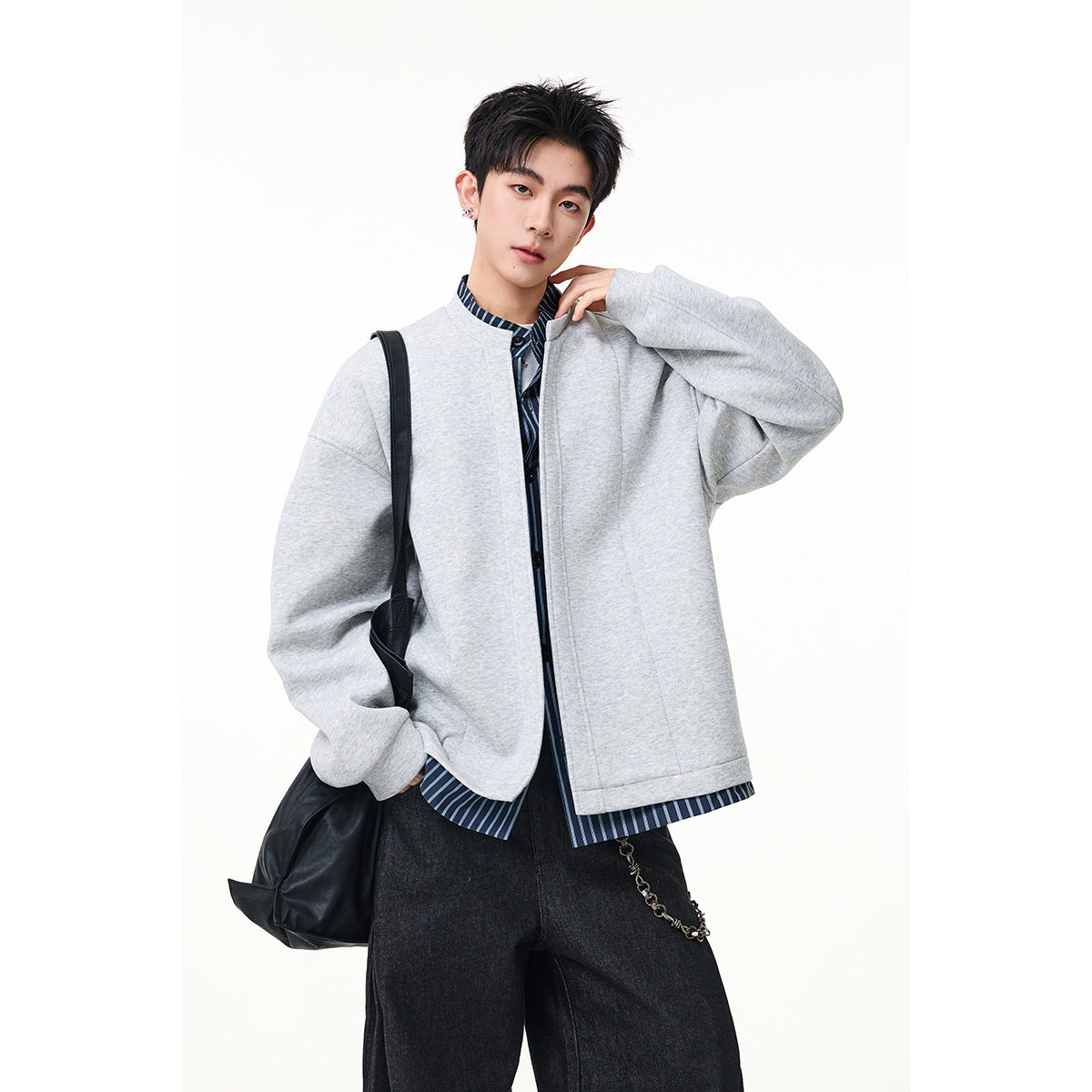 Model wearing a light gray oversized jacket over a blue striped shirt, with dark trousers.
