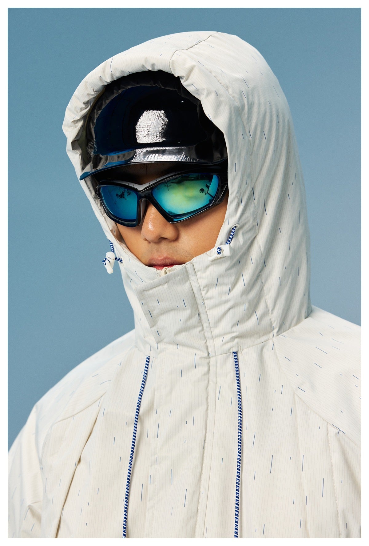Close-up of a model wearing the white patterned jacket with its hood raised and blue-and-white drawcords.