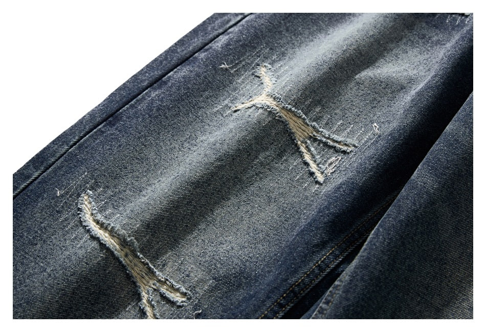 Close-up of dark washed jeans with two frayed distressed slashes and faded denim.