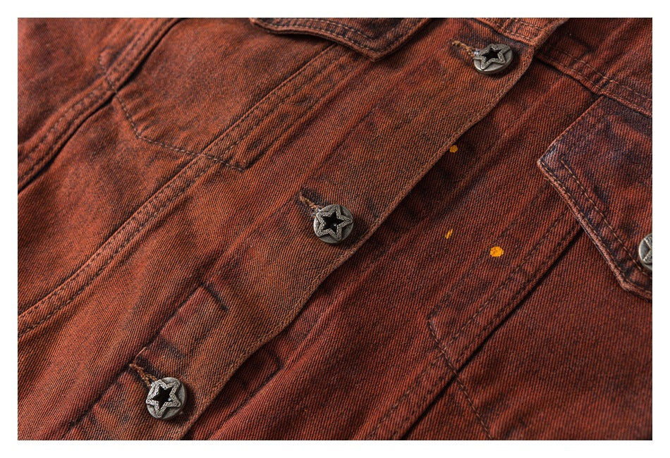 Close-up of a rust-red washed denim jacket front with star-shaped metal buttons, stitching and small yellow marks.