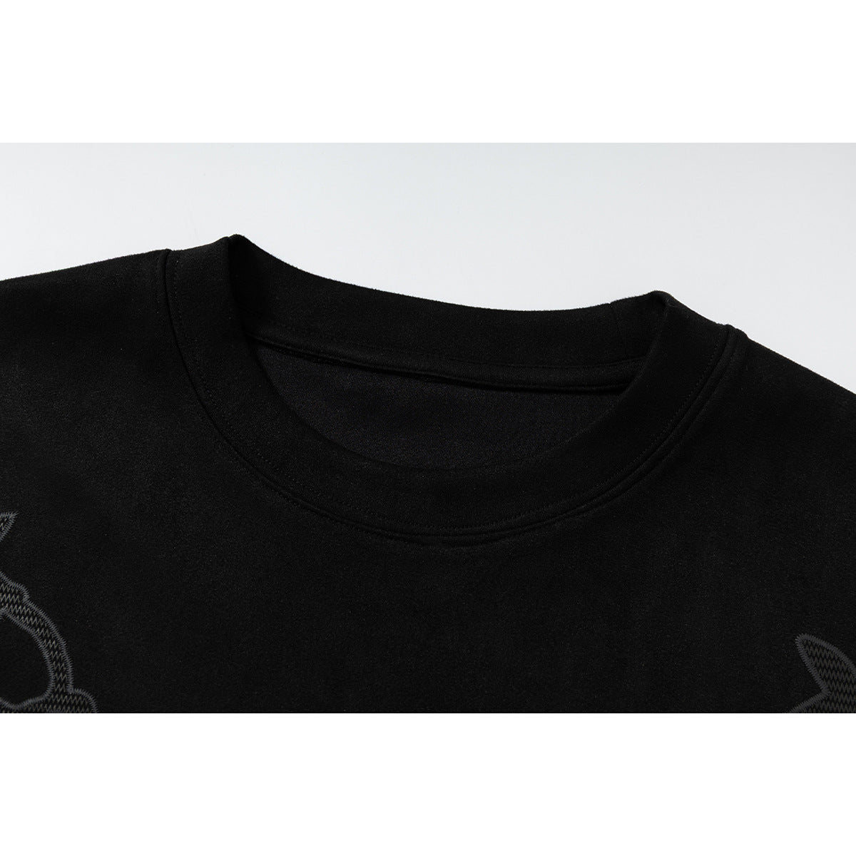 Close-up of a black crew-neck T-shirt collar with partial dark embroidered graphics at the edges.