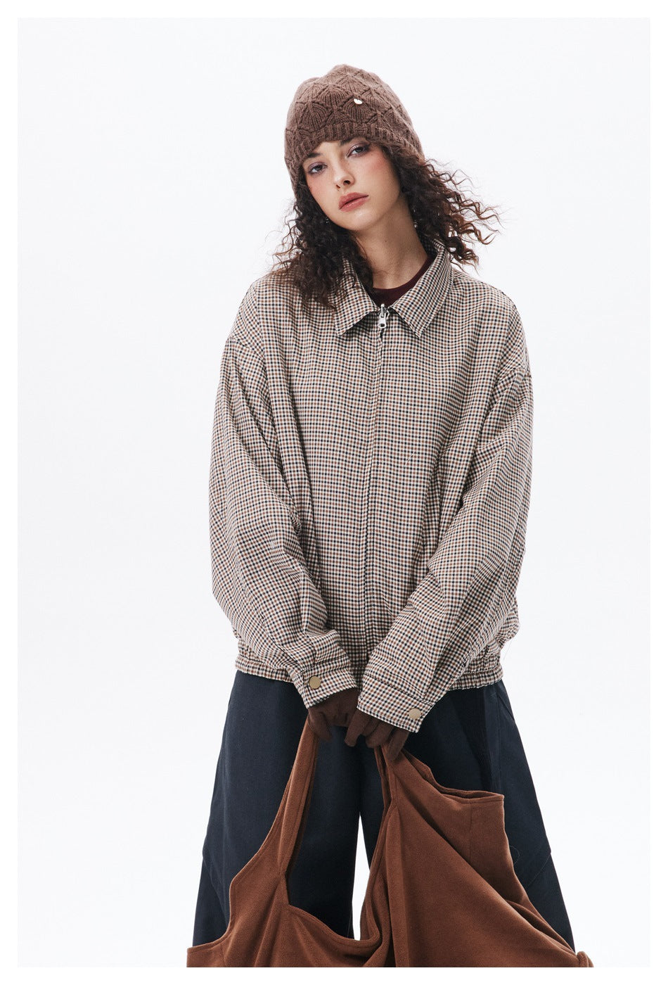 Model facing forward in a beige-and-brown check zip jacket with a pointed collar, navy trousers, and a brown knit beanie.