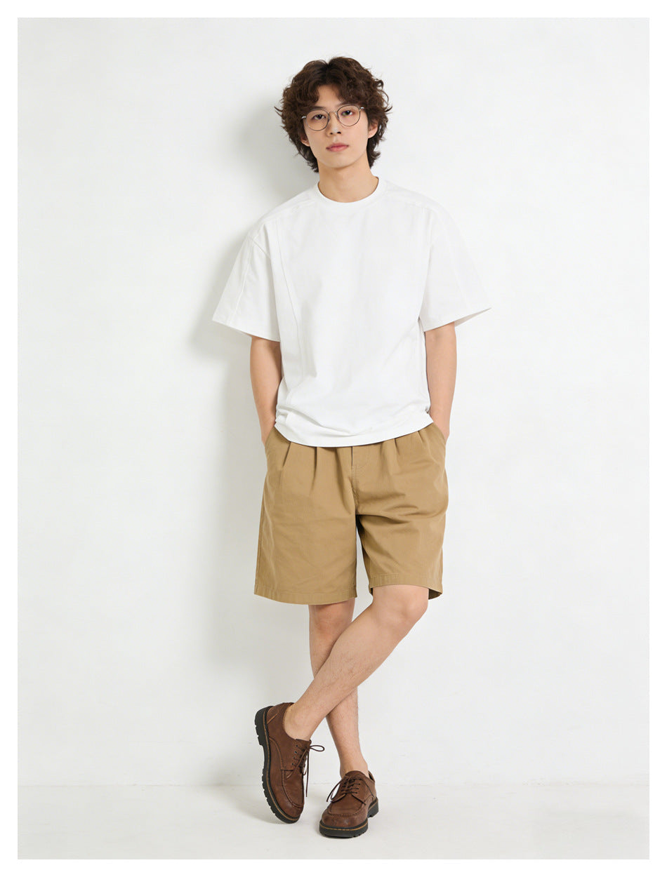 Model wearing a plain white short-sleeve T-shirt with tan shorts and brown lace-up shoes, full-length front view.