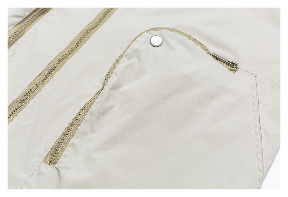 Close-up of a light beige garment with a zippered pocket flap, metal snap, and tan zippers.