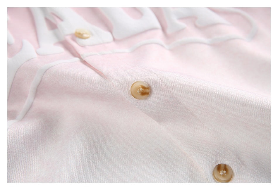 Close-up of pale pink shirt fabric, showing tan buttons and part of the raised white chest lettering.