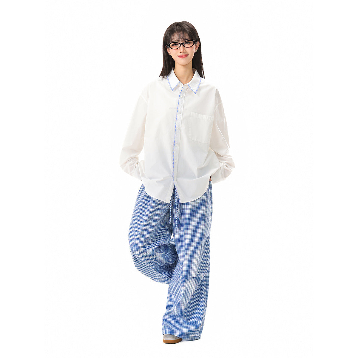 Model wearing a white long-sleeve button-up shirt with blue-trimmed collar and loose blue checked trousers.