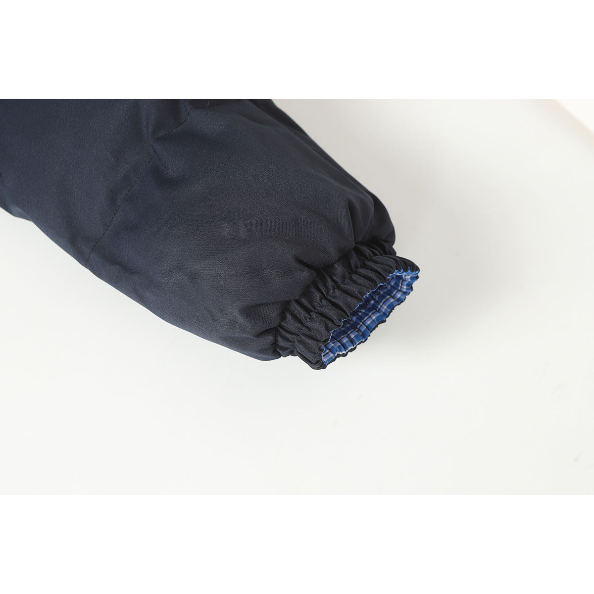 Close-up of a dark navy jacket sleeve ending in an elastic cuff with blue plaid lining.