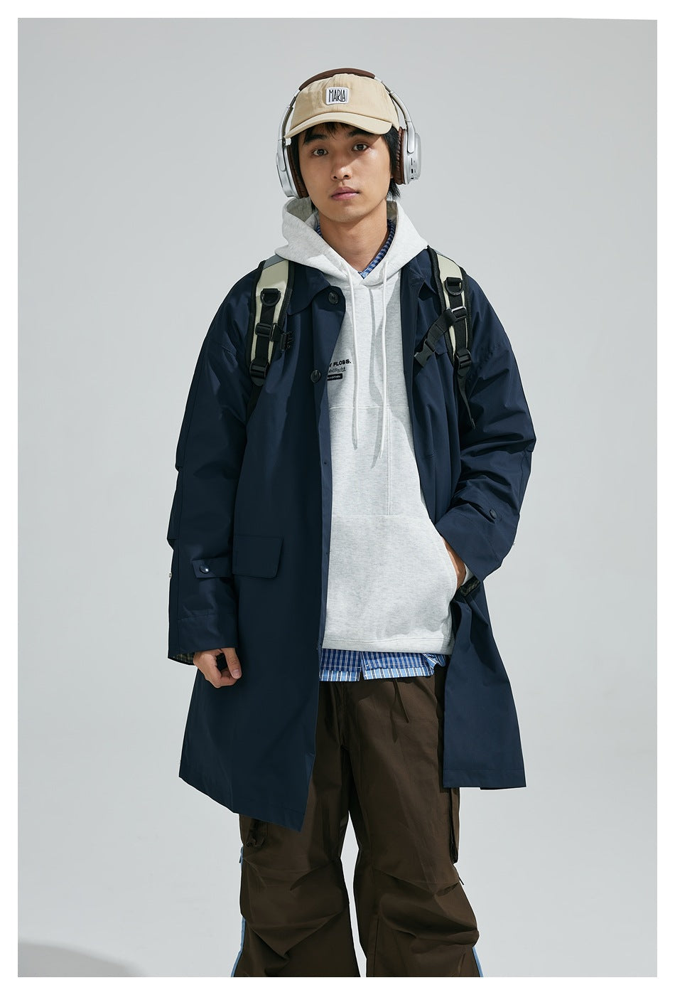 Model wearing an open navy long coat over a gray hoodie, with a backpack, shown from the front.