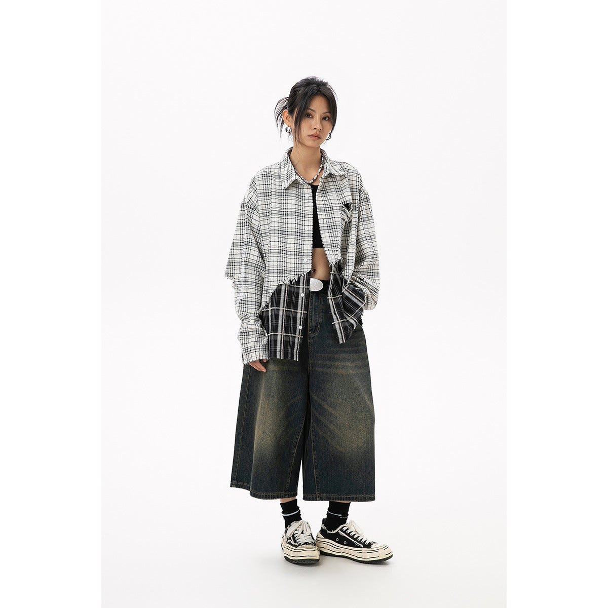 Model wearing an oversized black-and-white plaid shirt with a frayed hem and dark wide-leg cropped jeans, front view.