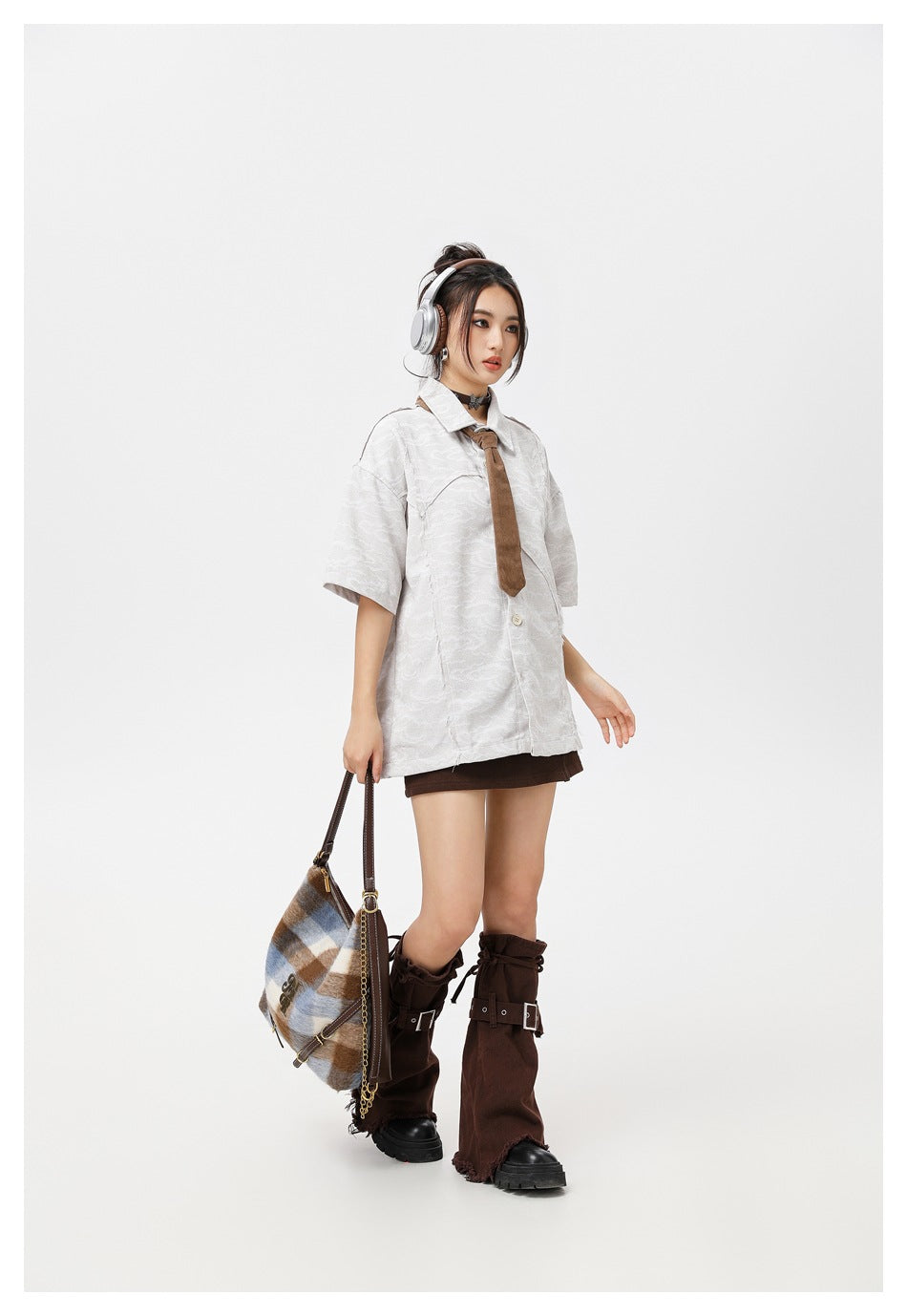 Model wearing a white patterned short-sleeve shirt with a brown tie and dark mini skirt, shown at an angle.