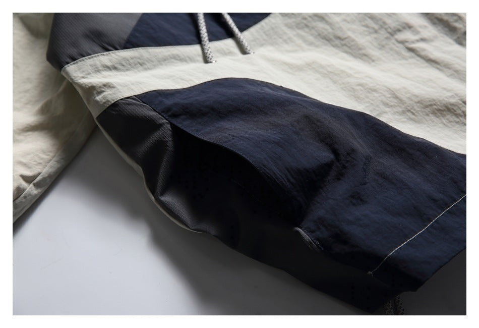 Close-up of a navy panel pocket on a light beige jacket, with contrasting fabric and stitched seams.