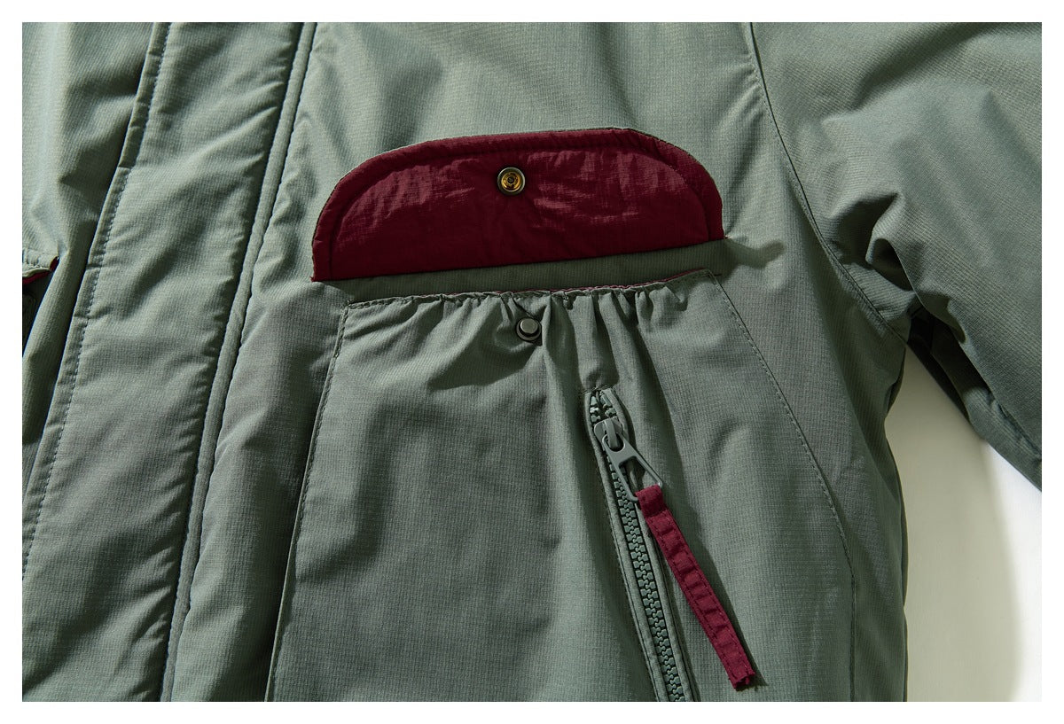 Close-up of a sage green jacket pocket with its burgundy-lined snap flap open and a vertical zipper.