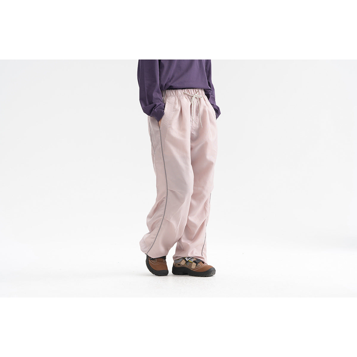 Side view of a model wearing pale pink loose drawstring pants with narrow side piping.