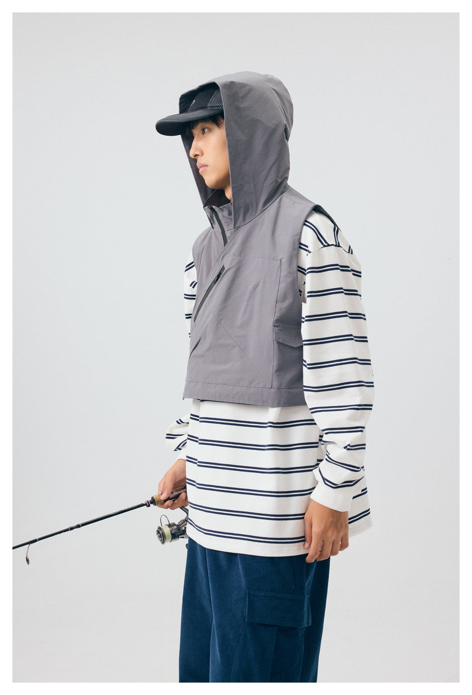Model wears the gray vest with its hood raised over a striped shirt; the vest has a diagonal chest zipper and side pocket.