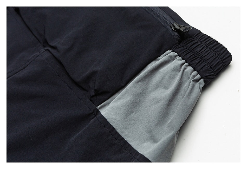 Close-up of black and gray garment panels, showing a zipper, gathered elastic waistband, and stitched seam.