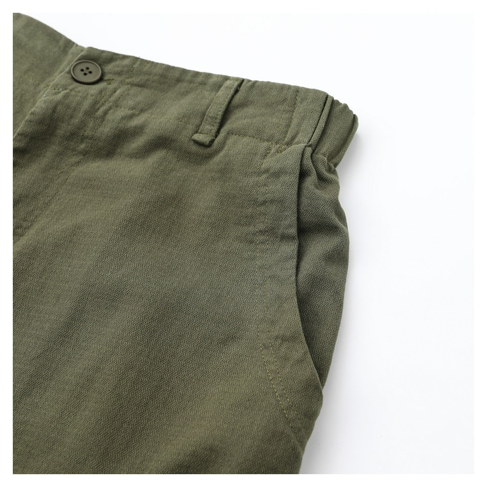 Close-up of olive pants showing a front pocket opening, waistband button, and belt loop.