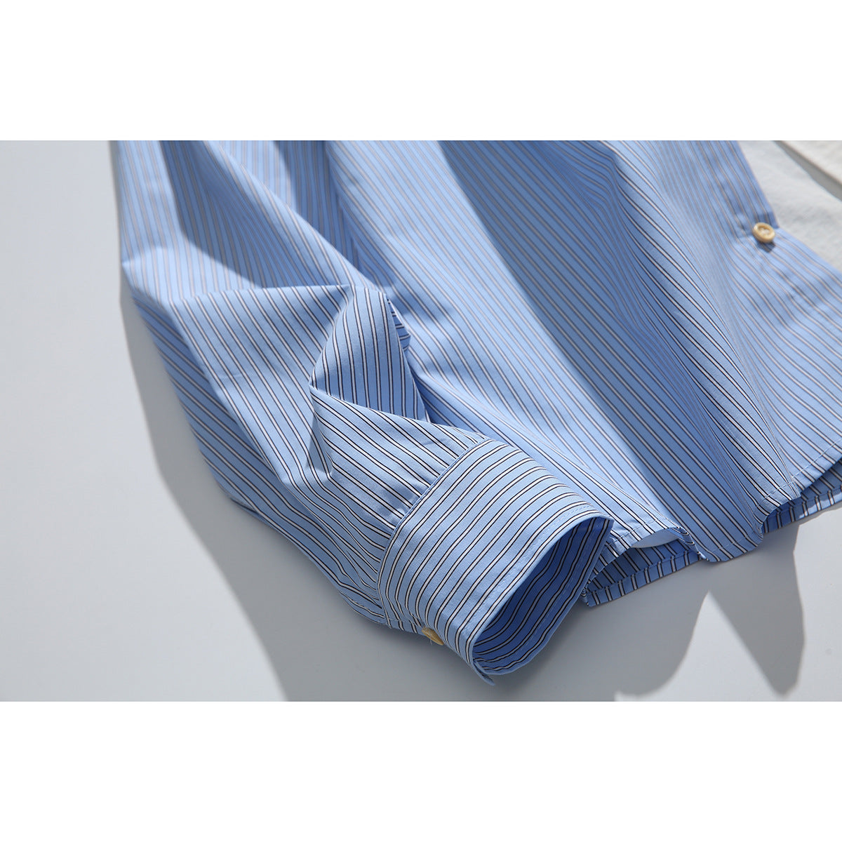 Close-up of the light blue striped shirt sleeve and turned-back cuff.