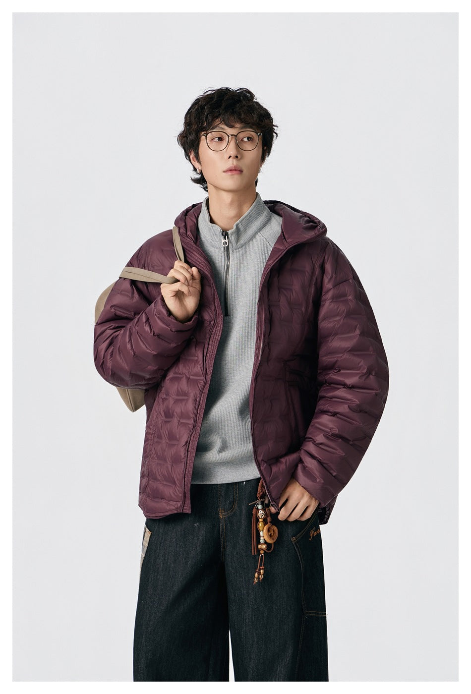 Model wearing a burgundy hooded quilted jacket over a gray zip-neck top, shown from the front.