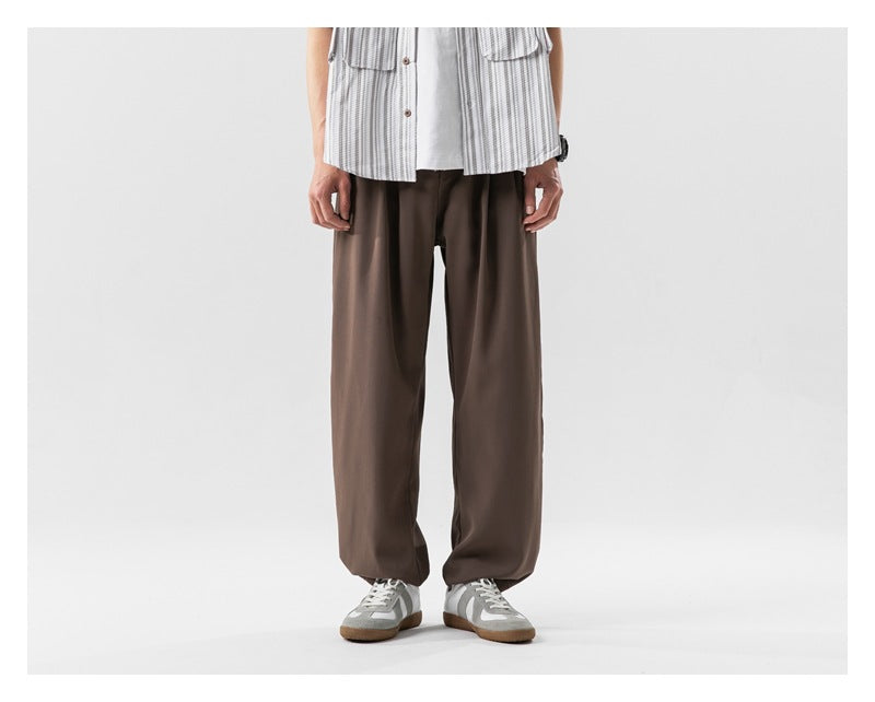 Front view of a model wearing loose brown wide-leg pants with a white striped shirt and gray sneakers.