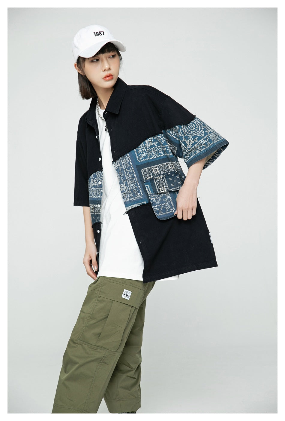 Angled view of a model wearing an oversized black shirt with blue bandana-print panels and olive cargo pants.