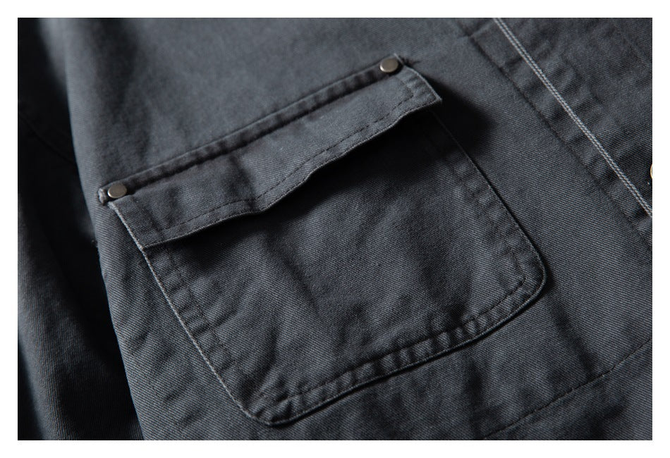 Close-up of a charcoal jacket pocket with a buttoned flap, stitched edges, and dark metal rivets.