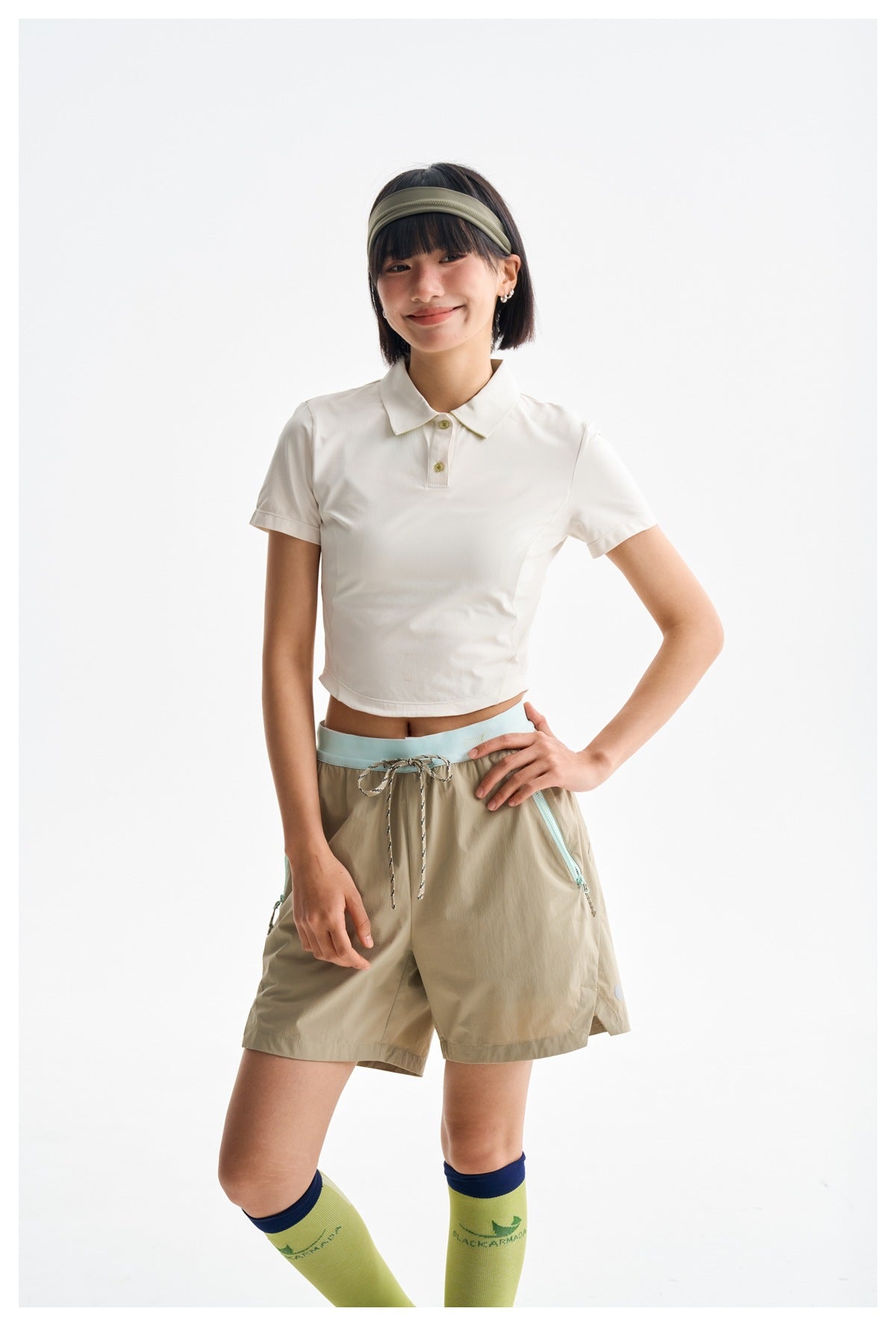 Closer view of a model in a white cropped polo and khaki shorts with pale blue waistband and pocket zips.