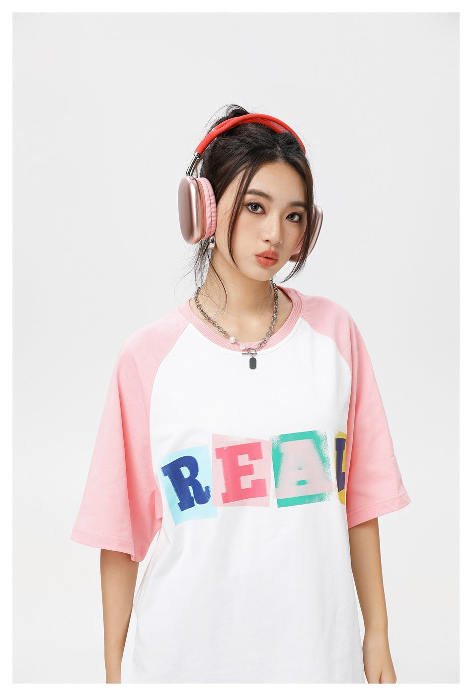 Close view of a model wearing a white T-shirt with pink raglan sleeves and colorful REAL lettering.