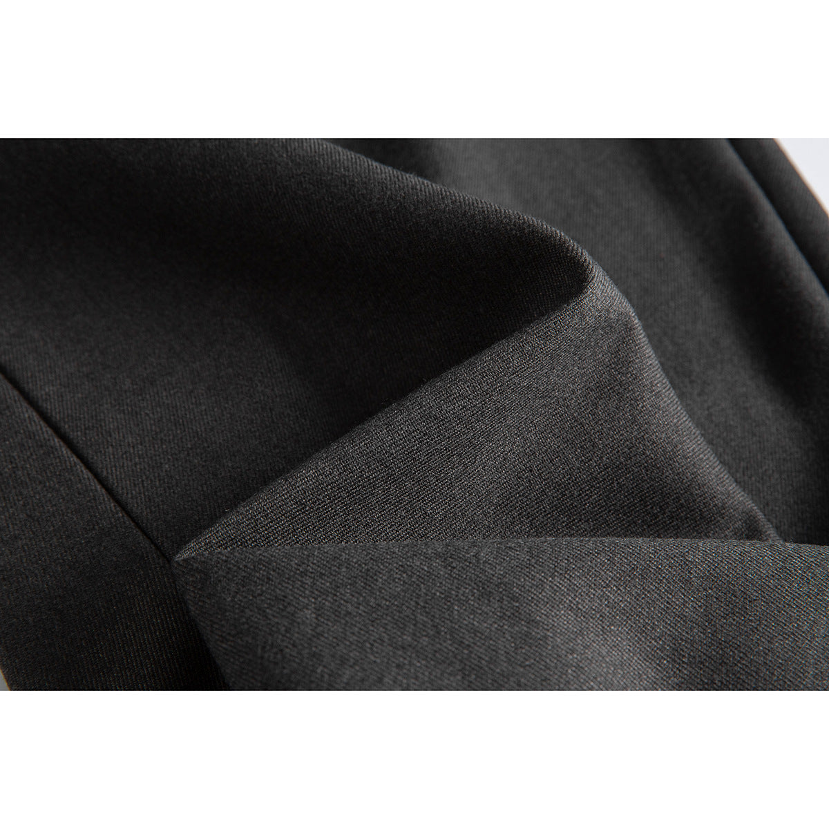 Macro view of dark charcoal trouser fabric folded to show its surface and drape.