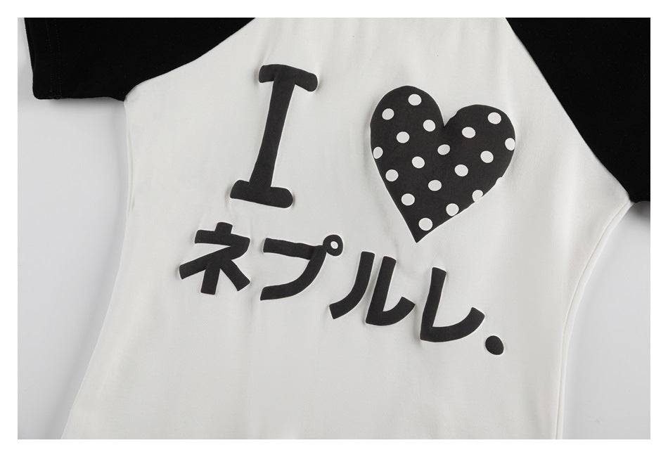 Close-up of a white shirt front with black raglan sleeves and a black polka-dot heart graphic with lettering.